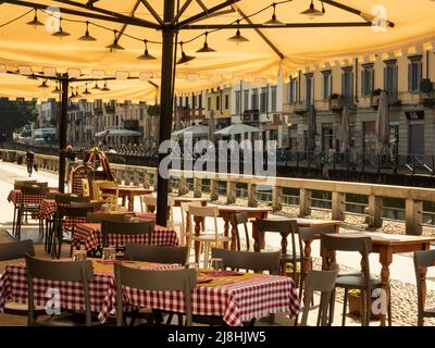 summer2020milan.tables d'une trattoria avec des nappes à carreaux typiques avec son soleil umbrella.in le fond le Naviglio de Milan le dimanche Banque D'Images