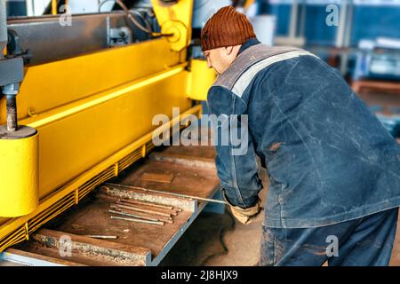 L'ouvrier coupe le métal sur la machine à guillotine mécanique dans le hall de production. Equipement industriel pour la découpe des métaux. Scène réelle. Flux de travail réel. Homme au travail. Banque D'Images