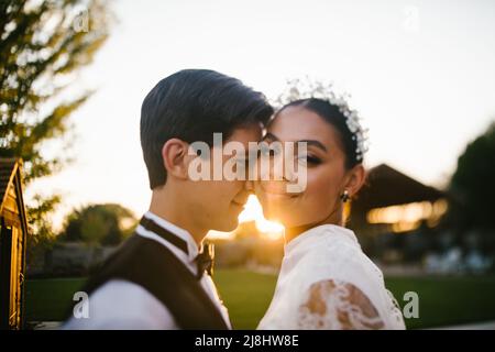 Mariée et marié de race mixte se blottir dans le coucher du soleil et lumière dorée Banque D'Images