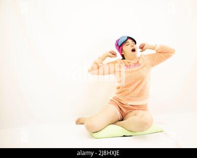 jolie jeune femme blanche asiatique portant un pyjama rose, bâillonne du sommeil et fatiguée, sur fond blanc Banque D'Images