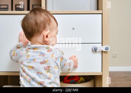 Bébé garçon se déporte d'un tiroir de cabinet avec sa main. L'enfant tient la poignée de la porte de l'armoire, petit enfant Banque D'Images