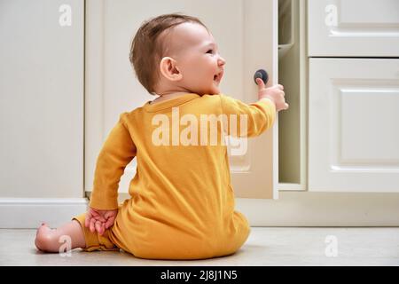 Bébé garçon se déporte d'un tiroir de cabinet avec sa main. L'enfant tient la poignée de la porte de l'armoire, petit enfant Banque D'Images