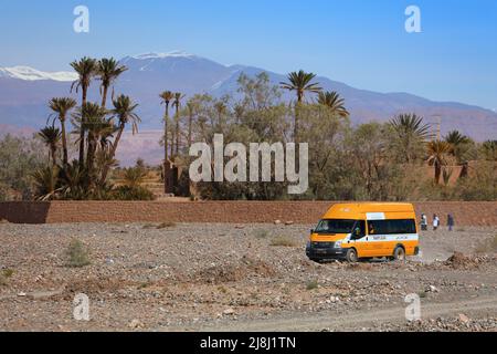 OUARZAZATE, MAROC - 18 FÉVRIER 2022 : le bus scolaire jaune navigue sur la route de la terre dans les zones rurales du Maroc avec les montagnes de l'Atlas en arrière-plan. Il a été financé par N Banque D'Images