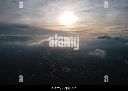 Vue aérienne depuis la haute altitude de la ville éloignée couverte de cumulus bouffieux qui volent avant la tempête au coucher du soleil. Point de vue de l'avion Banque D'Images