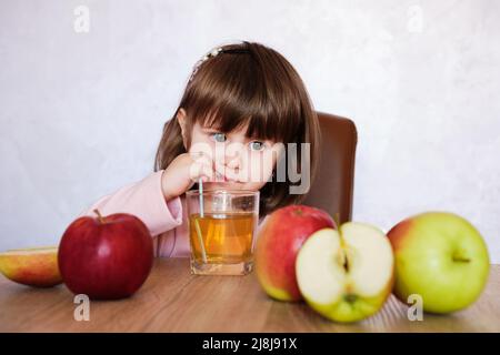 Une petite fille mignonne boit du jus de pomme avec de la paille à boire. Petite fille avec jus et pommes de fruits. Banque D'Images