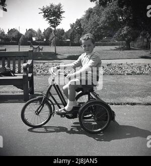 1950s, historique, un jeune garçon sur un tricycle sur un chemin dans un parc, Westgate-on-Sea, Margate, Kent, Angleterre, ROYAUME-UNI. Le tricycle semble être un tricycle junior TRIANG à cadre d'acier avec botte, qui a été fait par la principale compagnie britannique de jouets de l'époque, Lines Bros de Merton, Londres, Angleterre. Tri-Ang était la marque célèbre de l'entreprise, qui à un moment donné de cette époque, est devenue la plus grande compagnie de jouets au monde. Banque D'Images