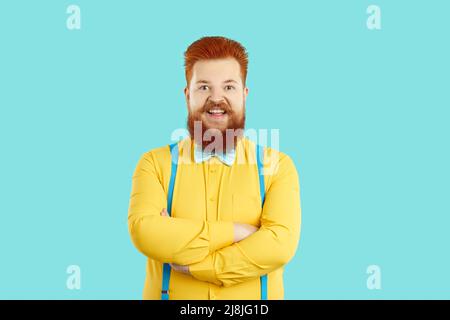 Joyeux homme gras barbu en chemise jaune et noeud papillon bleu debout avec ses bras pliés et souriant Banque D'Images