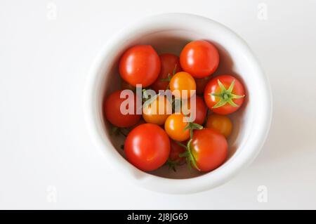 Tomates cerises aux couleurs vives dans un bol blanc avec un fond blanc vif, image prise du dessus. Banque D'Images