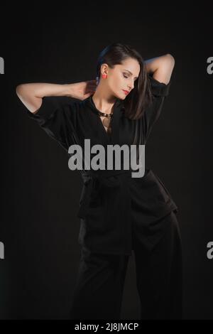 Brunette femme posant dans un kimono en soie noire avec des mains levées sur un fond noir Banque D'Images