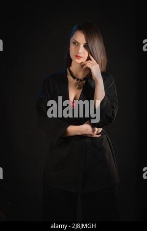 Studio de photo de la femme brune 30s dans un kimono noir sur fond noir Banque D'Images