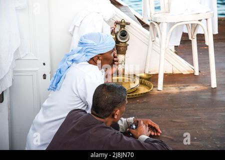 Deux membres d'équipage sur un bateau touristique du Nil Dahabiya se détendent avec un café sur le pont du bateau Banque D'Images