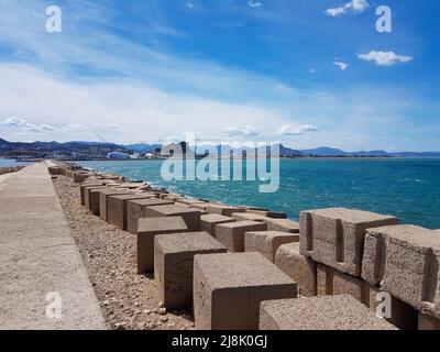 Blocs rectangulaires sur le mur du port de Denia surplombant la mer en face du port sous le ciel bleu ensoleillé, légèrement nuageux Banque D'Images