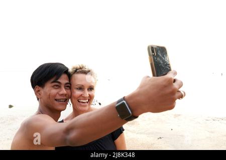 Couple multiculturel prenant un selfie avec un mobile sur la plage Banque D'Images