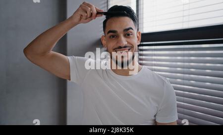 Arabian spaniard arab homme regardant l'appareil-photo peignant les cheveux avec la brosse à cheveux se préparer à la date jour de travail à la maison gars en T-shirt blanc matin beauté Banque D'Images