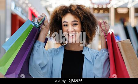 Gros plan contented african american girl tenant des sacs lumineux achats paquets profiter de réductions regardant l'appareil photo sourire largement Banque D'Images