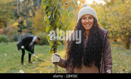 Gros plan jeune fille souriante heureuse debout à l'extérieur tenant la plantule en main homme creusant le trou pour planter l'arbre en arrière-plan bénévoles écoactivistes Banque D'Images