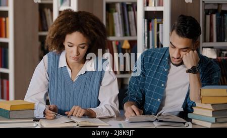 Deux étudiants gars et fille assis à la salle de classe de bureau écrit des notes dans le bloc-notes écrivant l'information de livre de lecture de manuel de jeunes hommes étudiant tombe Banque D'Images