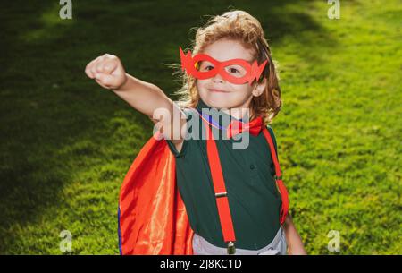 Super-héros enfant contre le champ vert de printemps en extérieur. Liberté et imagination enfants concept. Banque D'Images