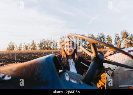 Une agricultrice latine se présente sur un vieux tracteur pour le conduire, au milieu de ses terres agricoles. Banque D'Images