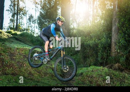 Homme sautant dans une forêt sur son VTT au lever du soleil Banque D'Images