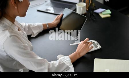 Gros plan, comptable féminin utilisant une tablette numérique et une calculatrice pour calculer ses comptes de ventes d'entreprise. Banque D'Images