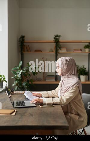 Vue verticale de côté de la jeune femme musulmane travaillant comme comptable faisant de la paperasse Banque D'Images