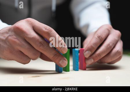 Photo conceptuelle des mains préparant une rangée de pierres domino. Effet Domino avec pierres colorées et espace de copie Banque D'Images
