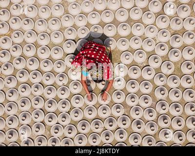 17 mai 2022, Brahmanbaria, Chittagong, Bangladesh : une femme arrange des milliers de pots d'argile avant d'être transportée pour vendre sur un marché à Brahmanbaria, Bangladesh. Les pots d'argile sont disposés à sécher sous le soleil brûlant avant qu'ils soient chargés dans des fours pour tirer comme une forme d'affaires de poterie. Environ 3 000 pots d'argile sont faits ici sur une base quotidienne et chacun d'eux est vendu pour 2 dollars (2$). La poterie, un commerce ancien, n'est faite que par les gens de la communauté ''Pal'' (Communauté Potters) de l'hindouisme. Pendant des siècles, ils ont vécu leurs compétences en poterie. Même aujourd'hui, leurs pots sont de Banque D'Images