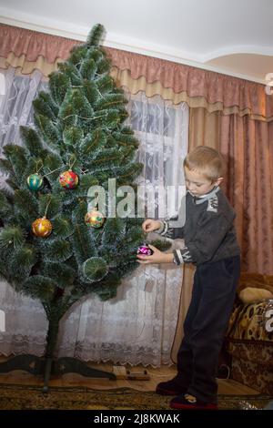 L'un d'entre eux décorera un sapin de Noël artificiel de jouets de balle dans la chambre Banque D'Images