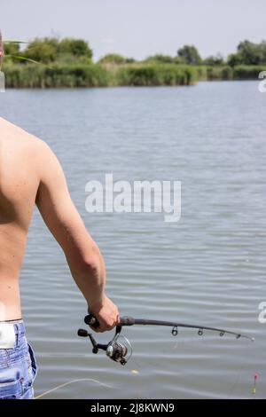 Jeune homme la pêche sur un lac de la voile au coucher du soleil Banque D'Images