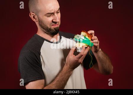 Le concept de restauration rapide et d'écologie. Un homme chauve avec une barbe ressemble déguisement à la garniture en plastique d'un hamburger. Arrière-plan Bourgogne. Banque D'Images