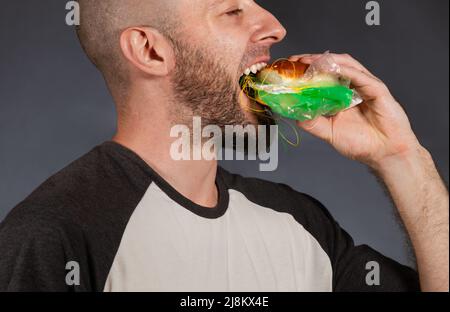 Pollution de l'environnement et industrie alimentaire. Gros plan d'un homme chauve avec une barbe, qui aime piquer dans un hamburger rempli de déchets et de ba Banque D'Images