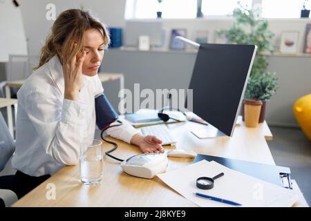 Une femme d'affaires fatiguée mesure la tension artérielle lorsqu'elle est assise sur le lieu de travail Banque D'Images