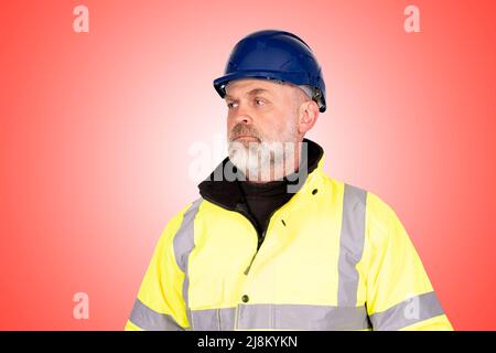 Un ouvrier de la construction dans un chapeau bleu et un manteau jaune de haute viz sur un fond rouge clair Banque D'Images