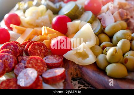 tomates cerises, poivrons doux, concombres marinés, ail mariné, olives, saucisse, différents fromages, bacon sur une assiette en bois. En-cas Banque D'Images