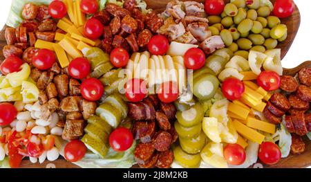 tomates cerises, poivrons doux, concombres marinés, ail mariné, olives, saucisse, différents fromages, bacon sur une assiette en bois. En-cas Banque D'Images