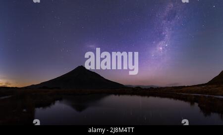 Le ciel nocturne sur le Mont Taranaki se reflète dans le tarn de Pouakai. Grimpeurs avec lampe torche près du sommet. Nouvelle-Zélande. Banque D'Images