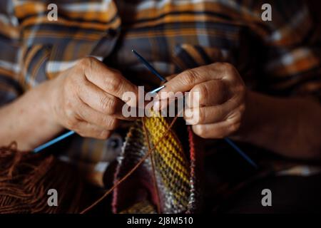 Les mains de femme inreconnaissables d'une femme âgée parlaient des vêtements colorés à carreaux. Fabrication d'une nouvelle écharpe ou d'un nouveau chandail Banque D'Images