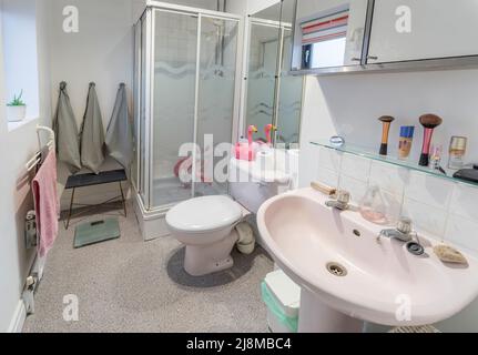 salle de bains des années 1980 avec cabine de douche d'angle, verre translucide à motifs, toilettes roses couplées et lavabo sur pied. Banque D'Images