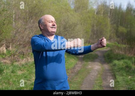 Coureur senior avec brassard s'étirant. Nature printanière. Un mode de vie sain à la vieillesse. Banque D'Images