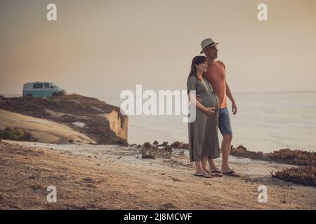 Couple enceinte sur une plage sauvage et leur chien attend un bébé Banque D'Images
