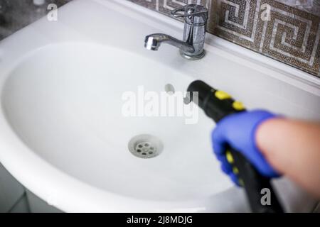 Nettoyage et désinfection du lavabo de la salle de bains à la vapeur chaude. Processus de nettoyage professionnel Banque D'Images