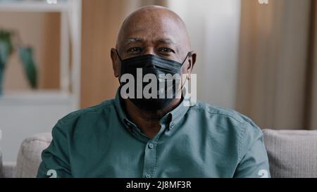 Portrait ancien solitaire africain dominican mature homme 60s grand-père mature senior homme triste patient pensif en noir masque médical à la maison à l'intérieur regardant Banque D'Images