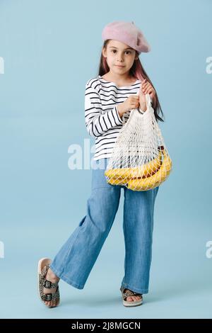 Tween fille à la mode dans un béret français tenant un sac à filet avec des bananes. Banque D'Images