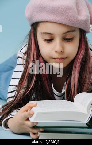 Gros plan d'une fille en Tween dans des livres de lecture de béret français, allongé sur le sol Banque D'Images