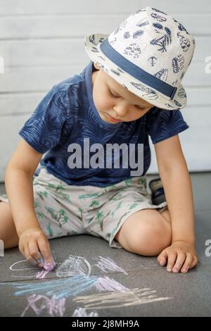 Petit garçon artiste 3-4 ans, dessine avec des crayons sur la chaussée. L'enfant est très concentré. Activités pour les enfants en plein air en été Banque D'Images