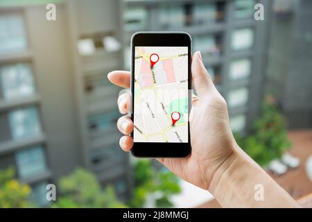 Homme tenant le smartphone avec la carte GPS pour la connexion réseau de destination d'itinéraire. Emplacement carte routière avec icônes GPS navigation et icône rouge emplacement. Banque D'Images