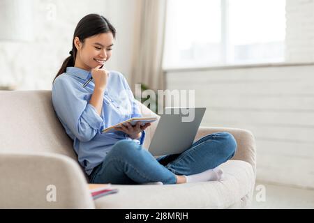 Femme asiatique enthousiaste assistant à des cours en ligne de la maison Banque D'Images