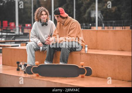 Guy et fille avec des planches à roulettes parlant assis dans le parc Banque D'Images