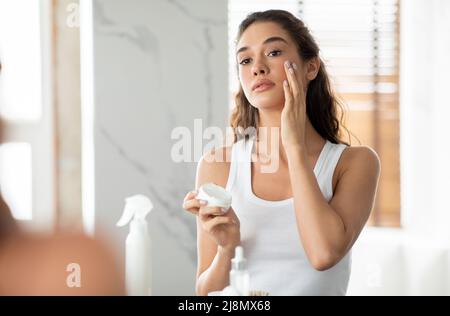 Magnifique Dame peau hydratante application de crème faciale dans la salle de bains moderne Banque D'Images